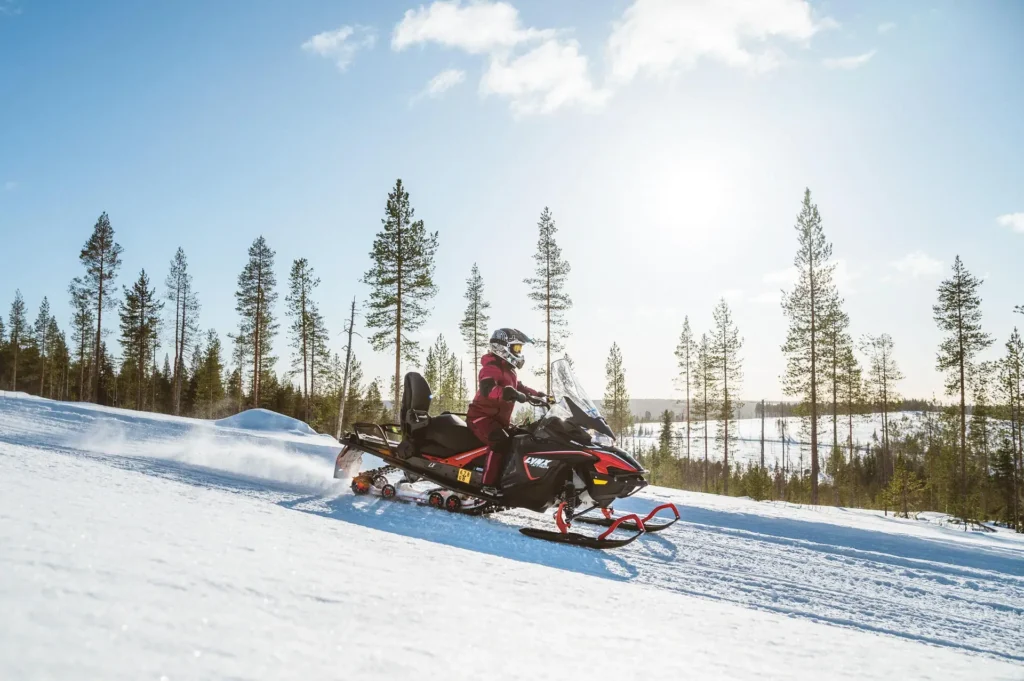 Snowmobile safari adventure riding through snowy pine forests in Lapland.