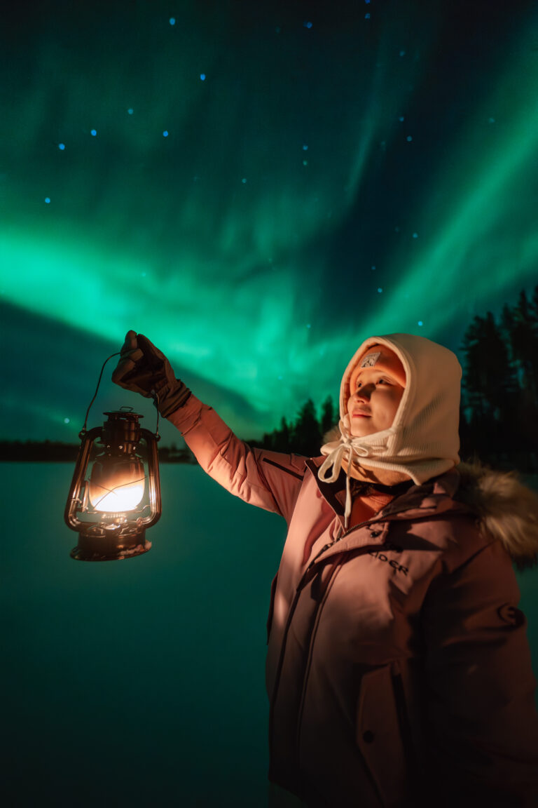 Woman holding a lantern beneath the vibrant Northern Lights in Lapland.