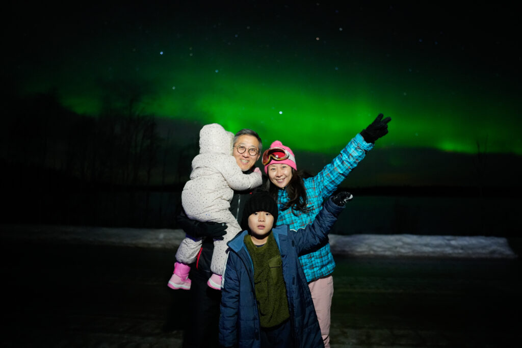 Family watching the Northern Lights illuminate the night sky in Lapland.