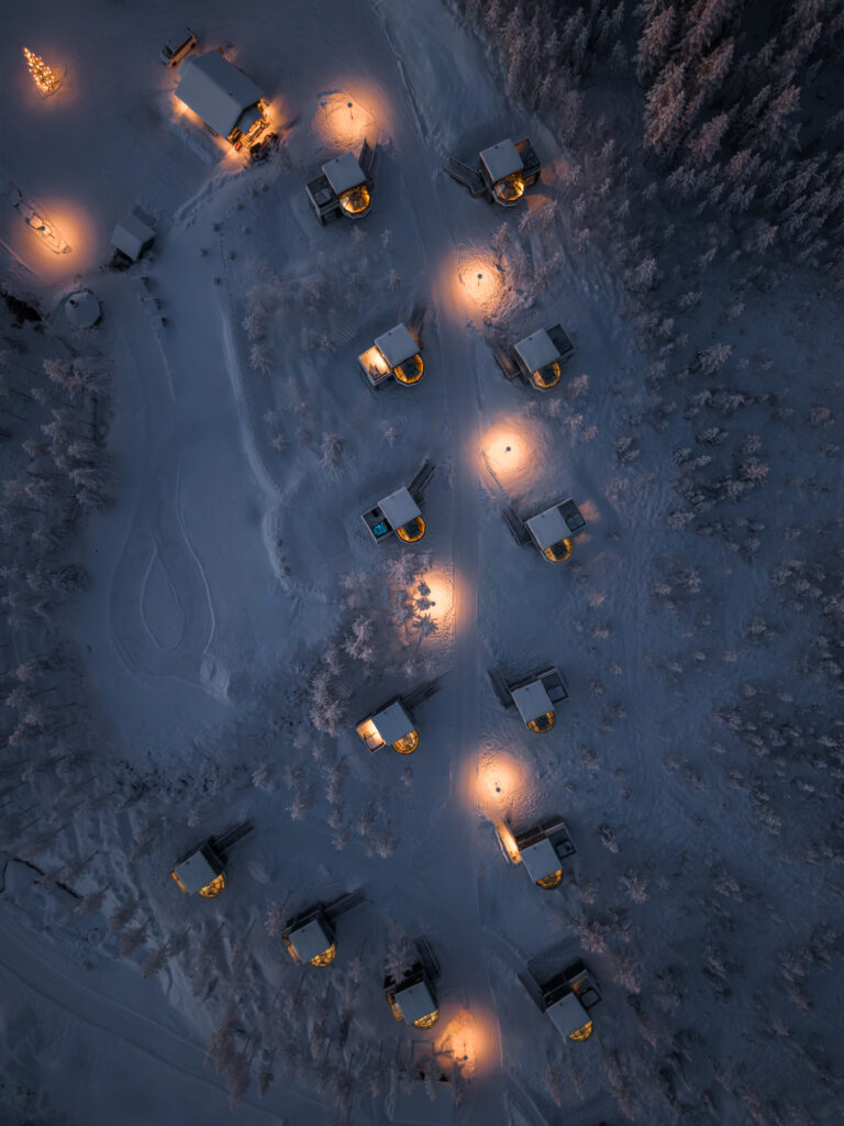 Aerial view of luxury illuminated glass igloos nestled in the snowy Lapland forest.