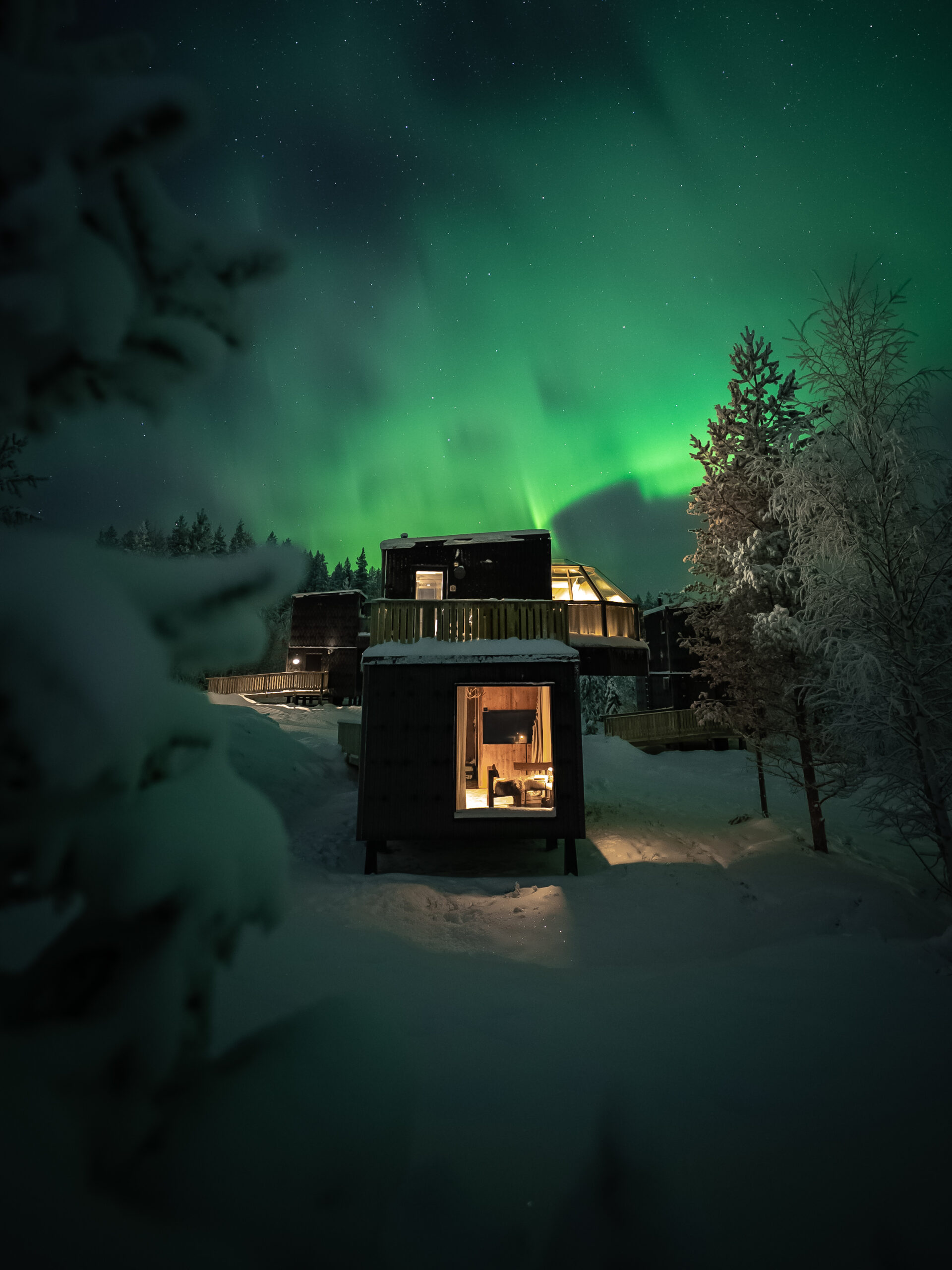 Luxury two-story glass igloo beneath glowing green Northern Lights.