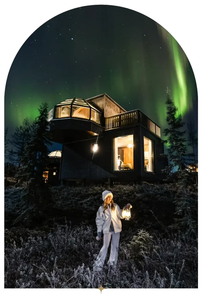 Guest holding a lantern outside the glass igloo under the Northern Lights.