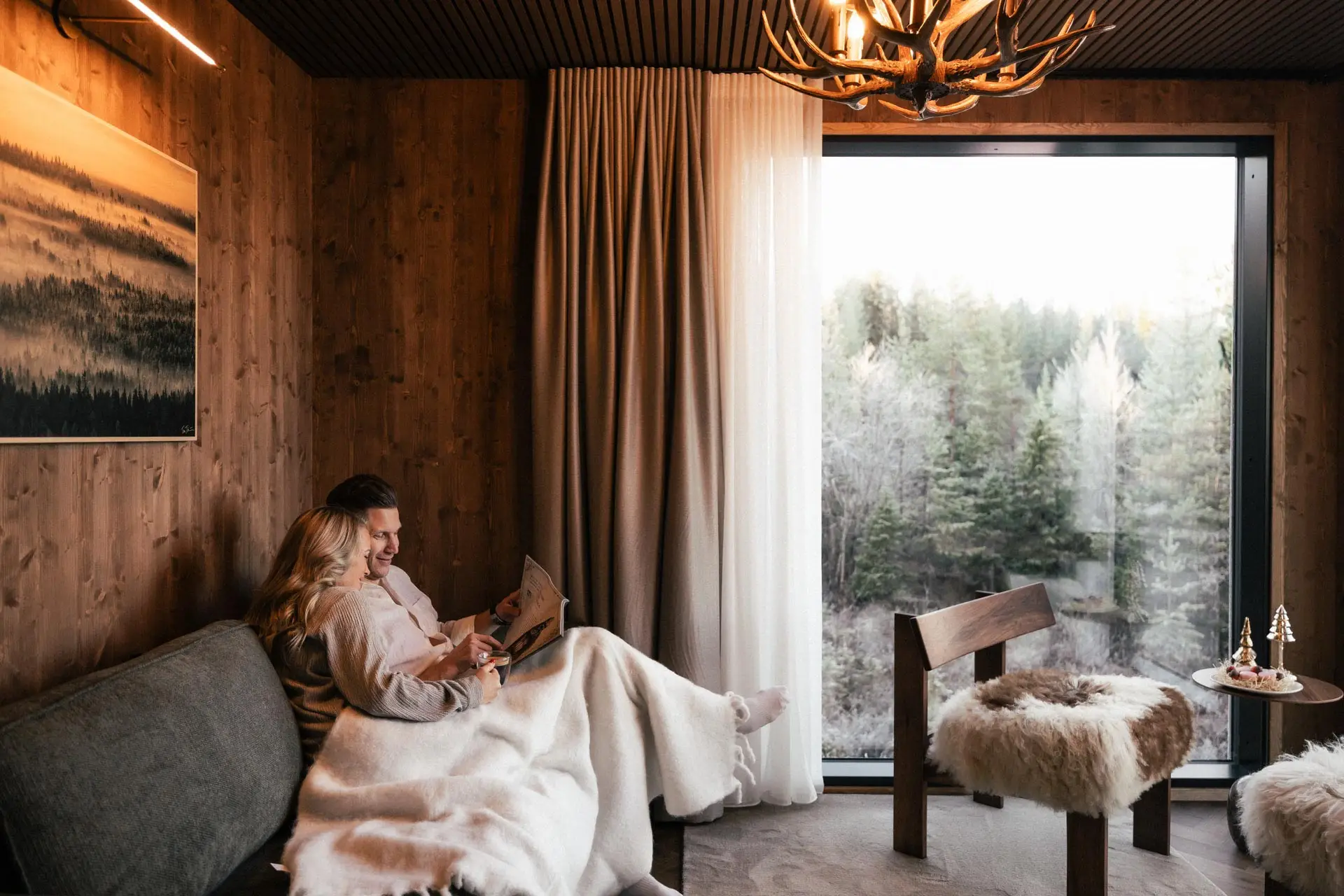 Couple relaxing in a luxury glass igloo lounge overlooking Arctic pine forests.